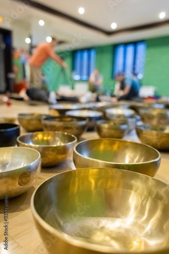 Close-up view of Tibetan singing bowls in a wellness studio with blurred background showing people engaging in a sound healing session or meditation activity photo