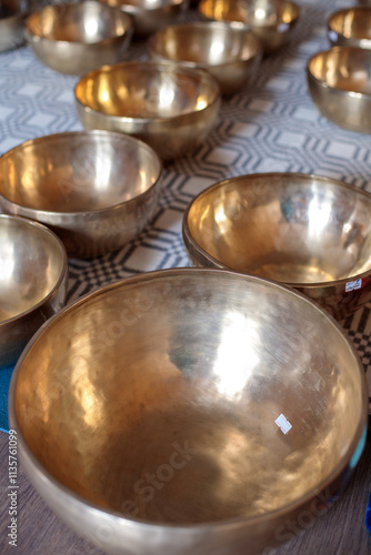 Golden Tibetan singing bowls arranged on a patterned surface, reflecting soft light, used in sound therapy and meditation practices for relaxation and healing photo