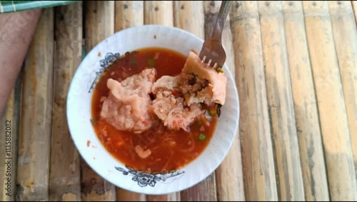 A man enjoying eating Bakso or pentol or meatballs and splitting meatball with soup with a spoon. Focus on meatball, photo