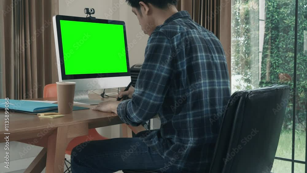 A man is sitting at a desk in front of a green computer monitor. A man is sitting at a desk in front of a green computer monitor.