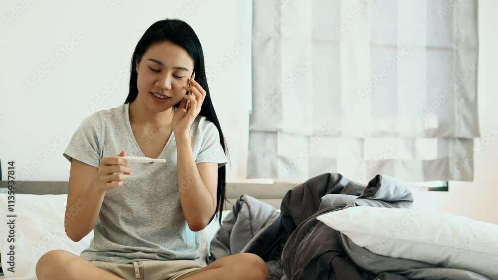 A woman is laying on a bed with a pregnancy test in her hand. She is smiling and she is happy