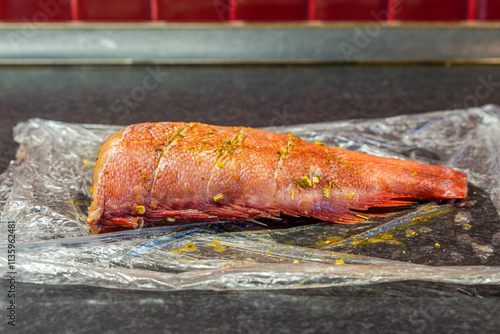 Marinated for baking fish red sea bass notothenia gutted without head with spices close-up on polyethylene view from the back.