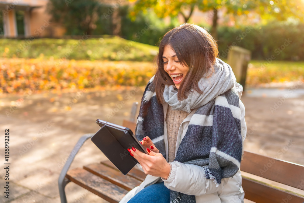 Obraz premium Woman laughing while using digital tablet in a park