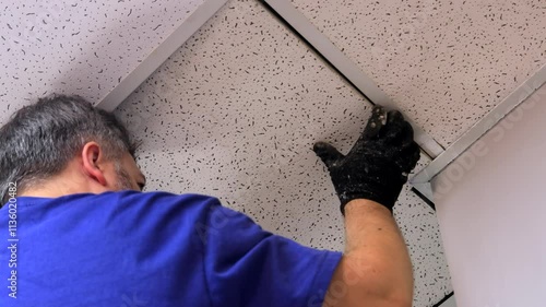 Electrician Installing Wires Under Suspended Ceiling Panels - Overhead Electrical Work with Sectional Ceiling Tiles