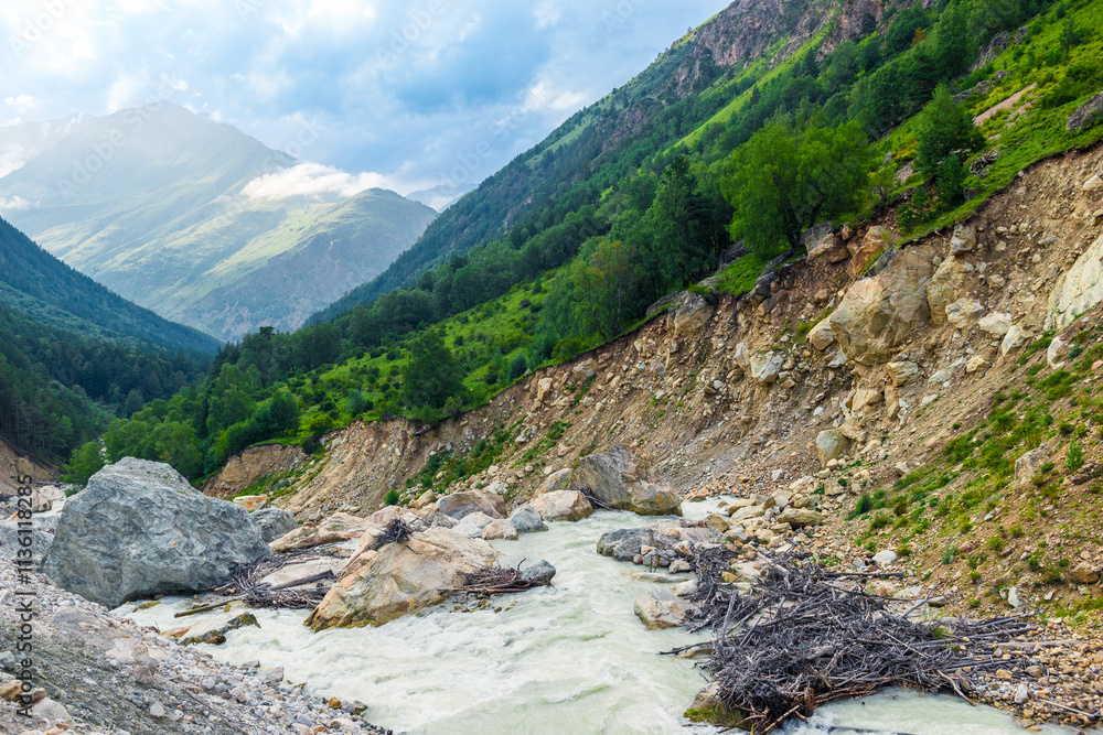 Picturesque mountain landscape of a stormy mountain river and a huge boulder among green mountains. Caucasus, Elbrus region Picturesque mountain landscape of a stormy mountain river and a huge boulder among green mountains. Caucasus, Elbrus region