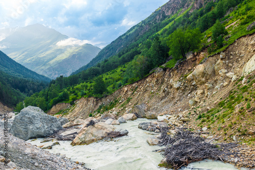 Picturesque mountain landscape of a stormy mountain river and a huge boulder among green mountains. Caucasus, Elbrus region