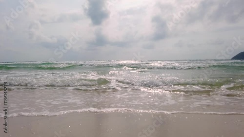 Foaming waves rushing onto a sandy sea beach in cloudy weather