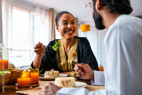 Happy beautiful young arab couple with emirati clothing having meal together at home