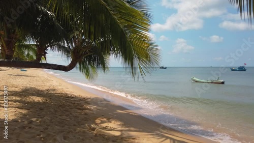 A sunny tropical beach in Vietnam with palm trees growing parallel to the ground and fishing boats bobbing on the waves