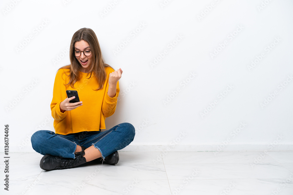 Young caucasian woman sitting on the floor isolated on white background surprised and sending a message Young caucasian woman sitting on the floor isolated on white background surprised and sending a message