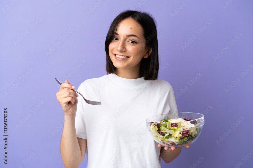 Young caucasian woman isolated on purple background holding a bowl of salad with happy expression Young caucasian woman isolated on purple background holding a bowl of salad with happy expression