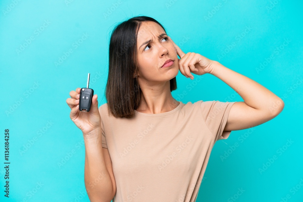 Obraz premium Young caucasian woman holding car keys isolated on blue background having doubts and with confuse face expression