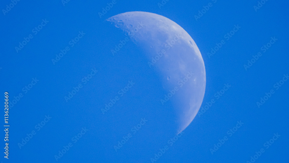 A crescent moon is visible against a clear blue sky. The moon is partially illuminated, showing some of its craters. A crescent moon is visible against a clear blue sky. The moon is partially illuminated, showing some of its craters.