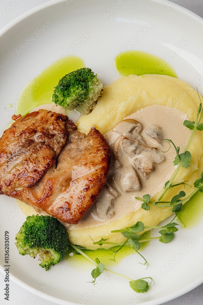 Grilled chicken breast is served with creamy mashed potatoes, steamed broccoli florets, fresh pea shoots, and a rich mushroom sauce. Restaurant or cafe menu, cookbook recipe Grilled chicken breast is served with creamy mashed potatoes, steamed broccoli florets, fresh pea shoots, and a rich mushroom sauce. Restaurant or cafe menu, cookbook recipe