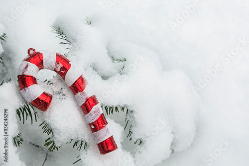 A Christmas tree toy in the form of a cane is located on a snow-covered spruce branch