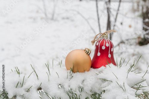 Christmas decorations - a golden ball and a red bell - lie in a snowdrift in the forest. New Year card