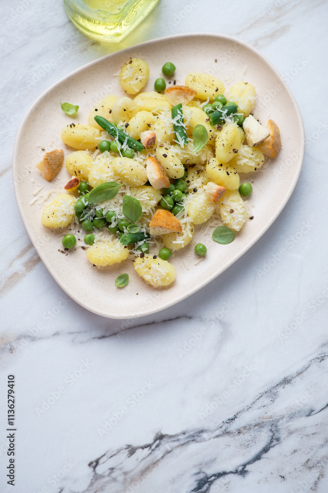 Potato gnocchi with cheese, green peas, beans and basil, vertical shot on a white stone background with space, high angle view Potato gnocchi with cheese, green peas, beans and basil, vertical shot on a white stone background with space, high angle view