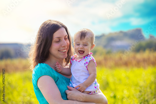 Obraz na płótnie Happy mother with daughter in a field on a sunny summer day. Mother holds her laughing little daughter in her arms w salonie