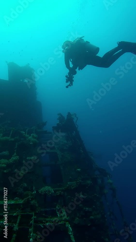 Vertical video, Scuba diver with camera in his hands looks at superstructure on wreckship of Salem Express ferry, Slow motion of diver swims in blue depths examines at sunken ship photo