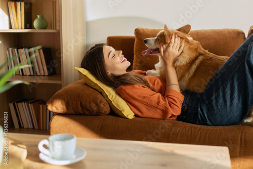 Fotografie Beautiful lady hugging and playing with her pretty Corgi dog, lying on couch at home