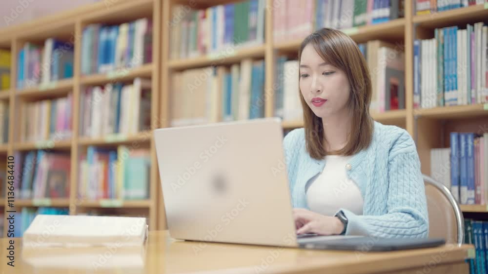 A woman is sitting at a table in a library, typing on a laptop. Concept of focus and concentration, as the woman is likely working or studying in a quiet environment A woman is sitting at a table in a library, typing on a laptop. Concept of focus and concentration, as the woman is likely working or studying in a quiet environment