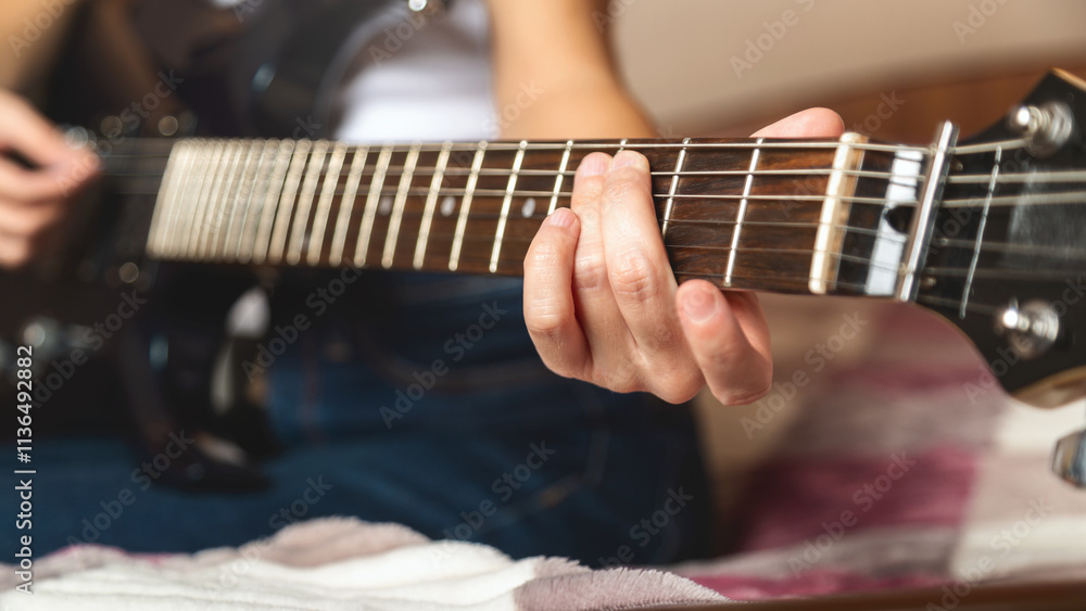 Fototapeta premium Close-up of a women playing a guitar on a bed. Guitar strings visible. Relaxed atmosphere with an emphasis on music. A woman plays an electric guitar.