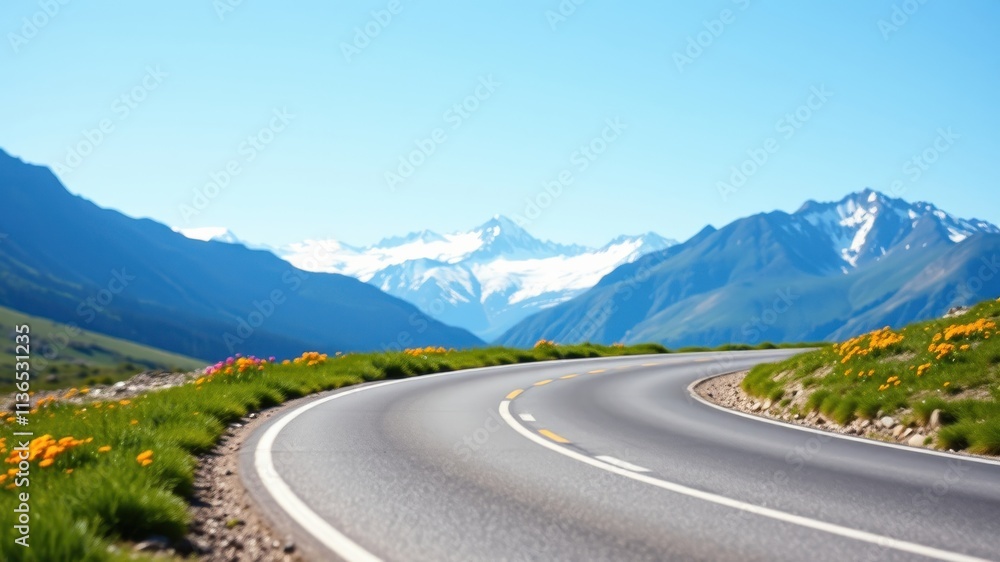 Fototapeta premium Asphalt road curving gently through alpine meadow landscape with snow-capped mountains in the background