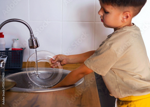 Funny 5 yearold boy is washing dishes standing at the sink. Housework assistant, the concept of work. photo