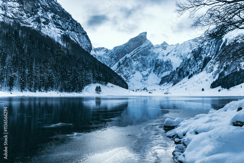 Frozen alpine lake with black ice surrounded by snow-covered mountains that reflects on the ice, Seealpsee, Switzerland