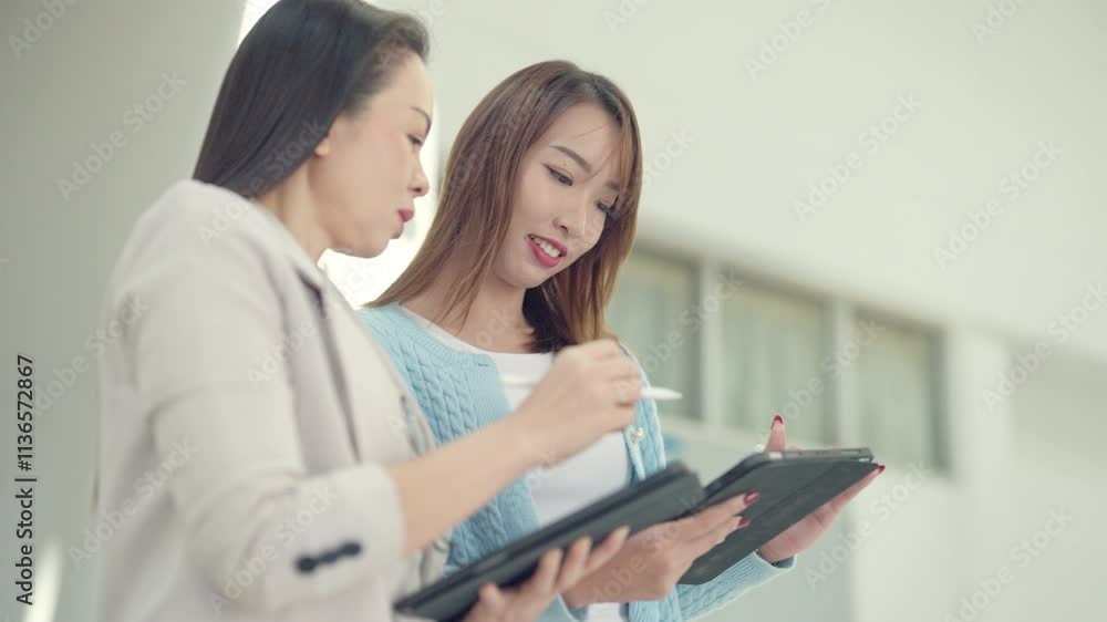 Two women are looking at a tablet and writing on a piece of paper. They seem to be discussing something important