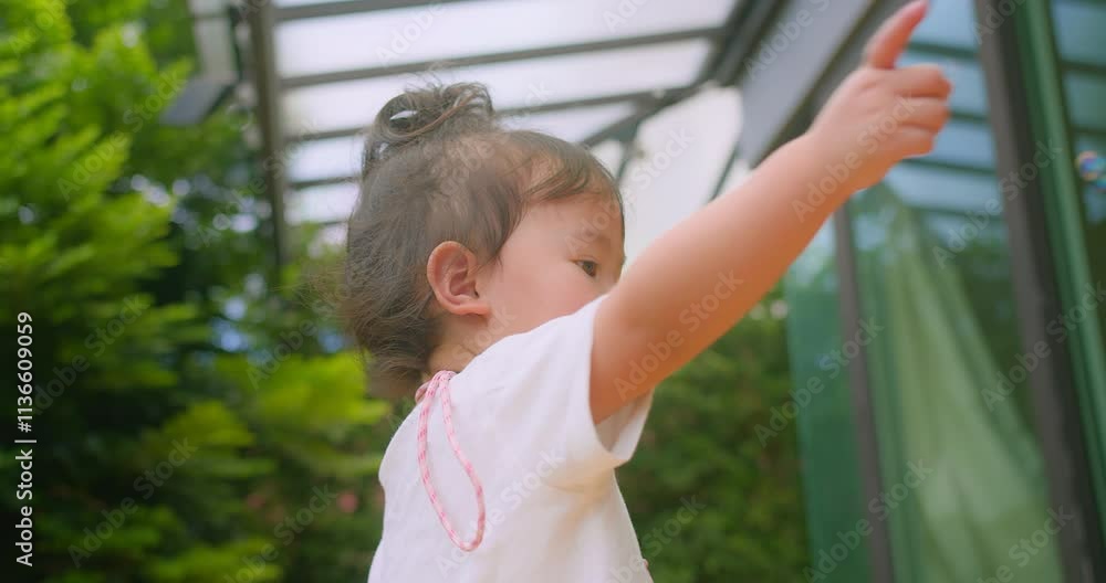 A young Asian child girl enjoying a sunny day outside surrounded by floating soap bubbles in Garden lush greenery in background, capturing the innocence and joy of childhood in natural light. A young Asian child girl enjoying a sunny day outside surrounded by floating soap bubbles in Garden lush greenery in background, capturing the innocence and joy of childhood in natural light.