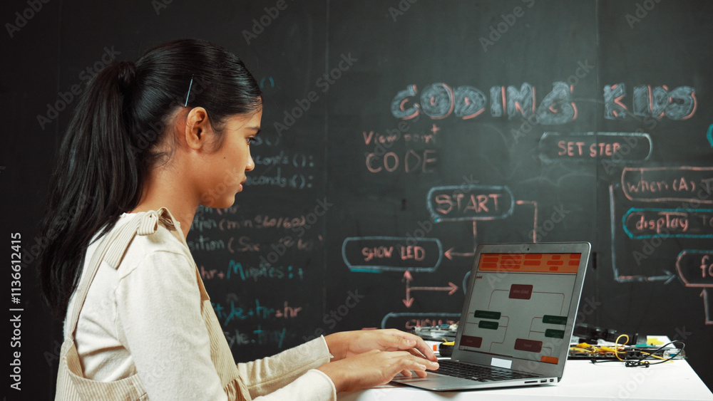 Highschool girl writing code or engineering prompt while attend in STEM technology class. Teenager coding or programing system while looking at computer screen in front of blackboard. Edification. Highschool girl writing code or engineering prompt while attend in STEM technology class. Teenager coding or programing system while looking at computer screen in front of blackboard. Edification.