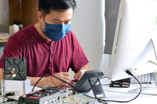 computer technician wearing a mask A motherboard repairman is using an IC meter to find faults on the motherboard to repair on his table. modern board repair technician photo