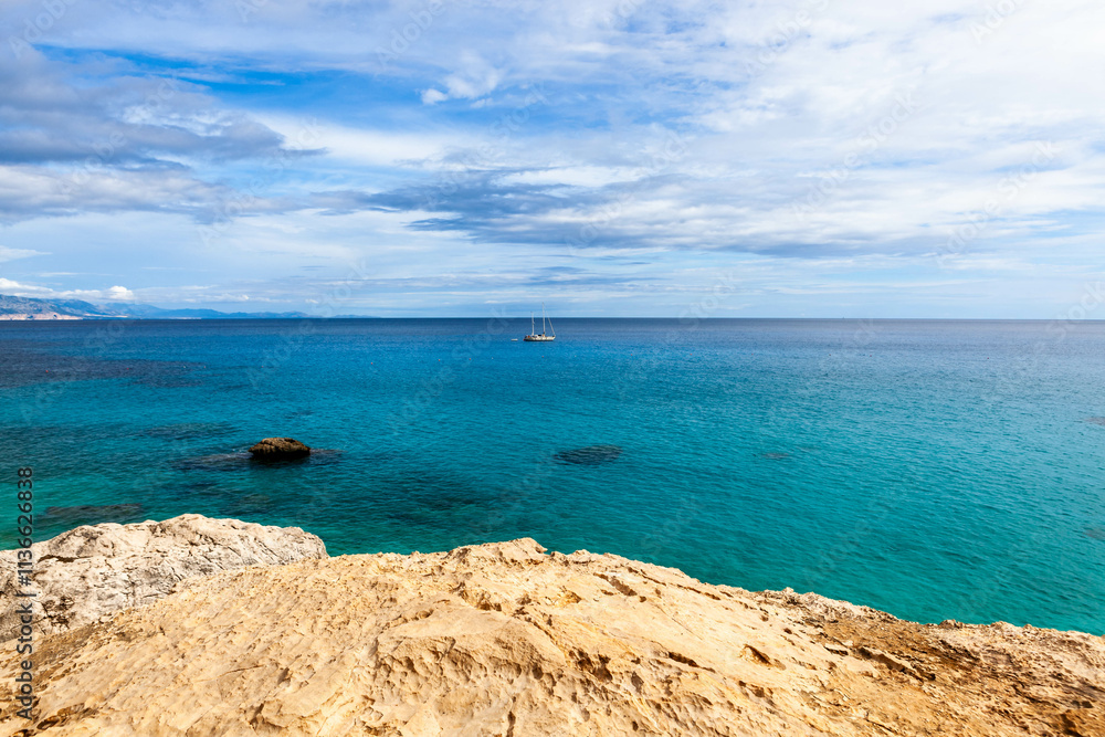 Fototapeta premium Sardinia. Italy. Crystal clear Mediterranean sea, beautiful rocks and white sailboat. Cala Goloritze, Baunei area, Sardinia, Italy.