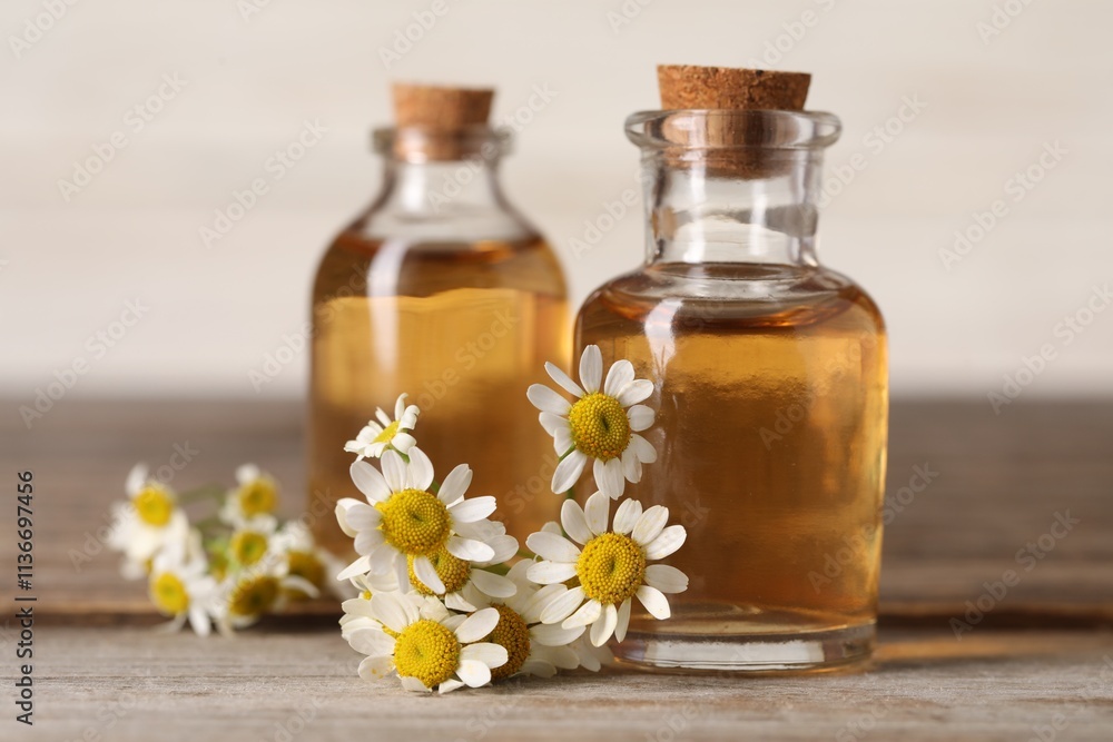 Bottles of essential oil and chamomile flowers on wooden table, closeup Bottles of essential oil and chamomile flowers on wooden table, closeup
