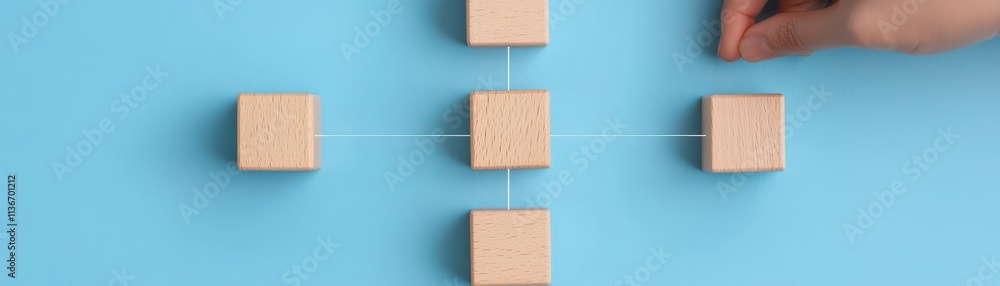 A hand is positioning wooden blocks on a blue background, illustrating a concept of connection or organization in a simple, minimalist design. A hand is positioning wooden blocks on a blue background, illustrating a concept of connection or organization in a simple, minimalist design.