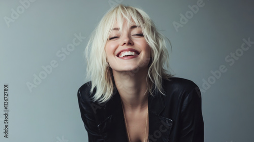 Smiling woman with blonde hair poses confidently in a stylish outfit against a neutral background