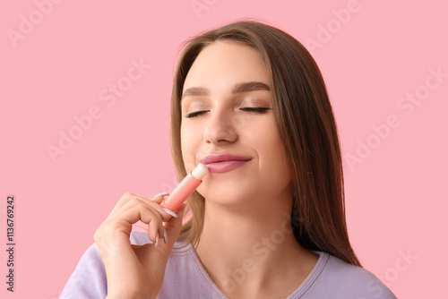 Beautiful young woman with lip balm on pink background photo