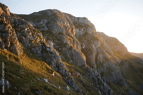 A dramatic mountain ridge with steep, rocky slopes, bathed in the warm light of the setting sun photo