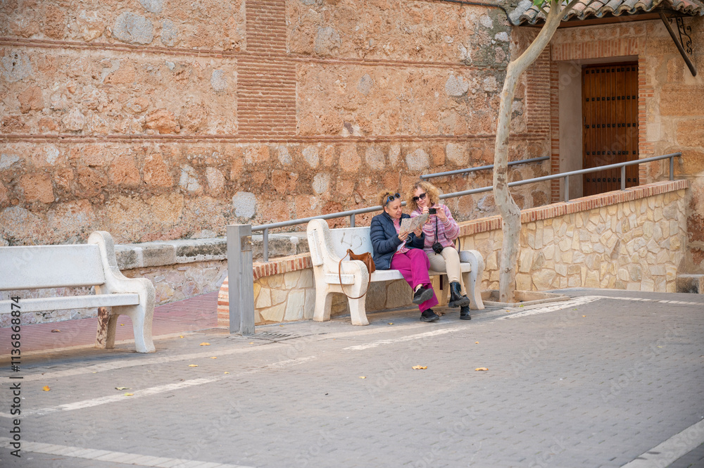 Obraz premium Two women sitting on a bench, reading a map during a city tour in Spain