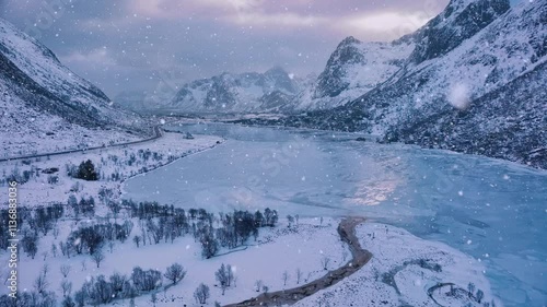 Aerial view of frozen lake in snowy mountains in winter at sunset. Lofoten islands, Norway. Top drone view of fjord in snowfall, frosted sea coast, reflection, ice, snowy rocks, purple sky with clouds