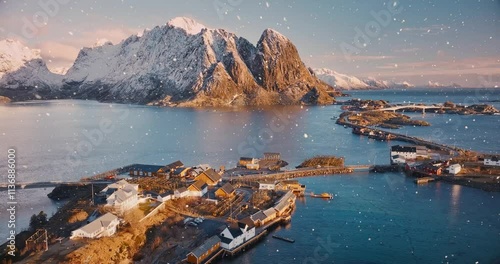 Aerial view of snowy mountains, islands with rorbuer houses, sea, bridge, road, sky with clouds at sunrise in snowfall winter. Top drone view of Reine and Hamnoy village, Lofoten islands, Norway