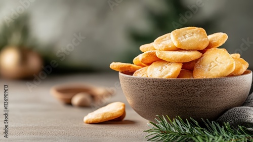 A rustic bowl filled with golden crackers set against a festive background with fir branches, perfect for a cozy holiday setting or snack inspiration stock image. photo