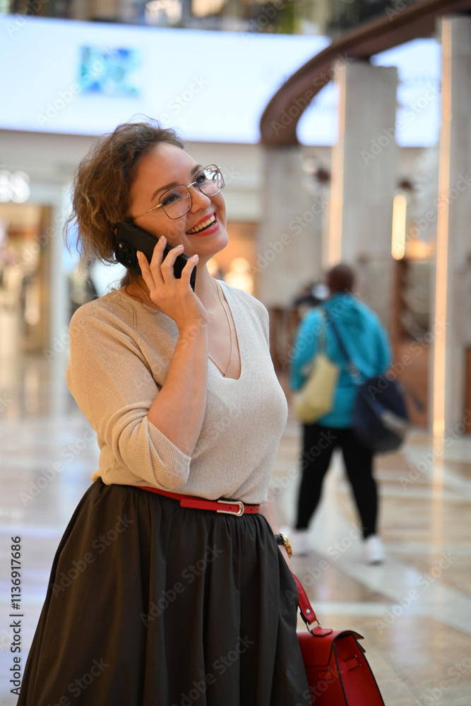 Fototapeta premium A young woman of European appearance is talking on the phone in a shopping mall