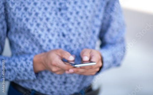 A man is holding a cell phone in his hand. He is wearing a blue shirt with a pattern