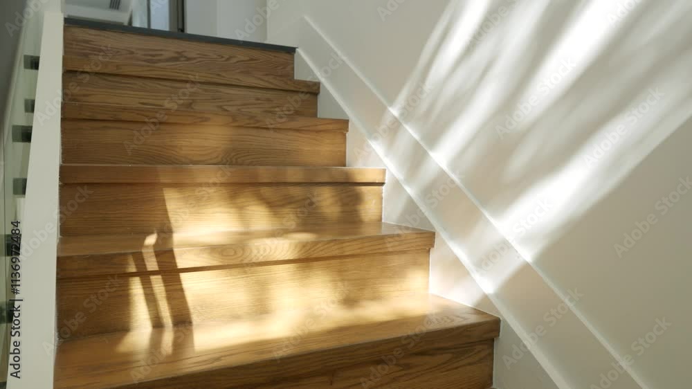 Modern staircase with wooden steps and glass railing. Sunlight casting shadows on steps and creating interesting play of light and shadow. Contemporary interior Modern staircase with wooden steps and glass railing. Sunlight casting shadows on steps and creating interesting play of light and shadow. Contemporary interior
