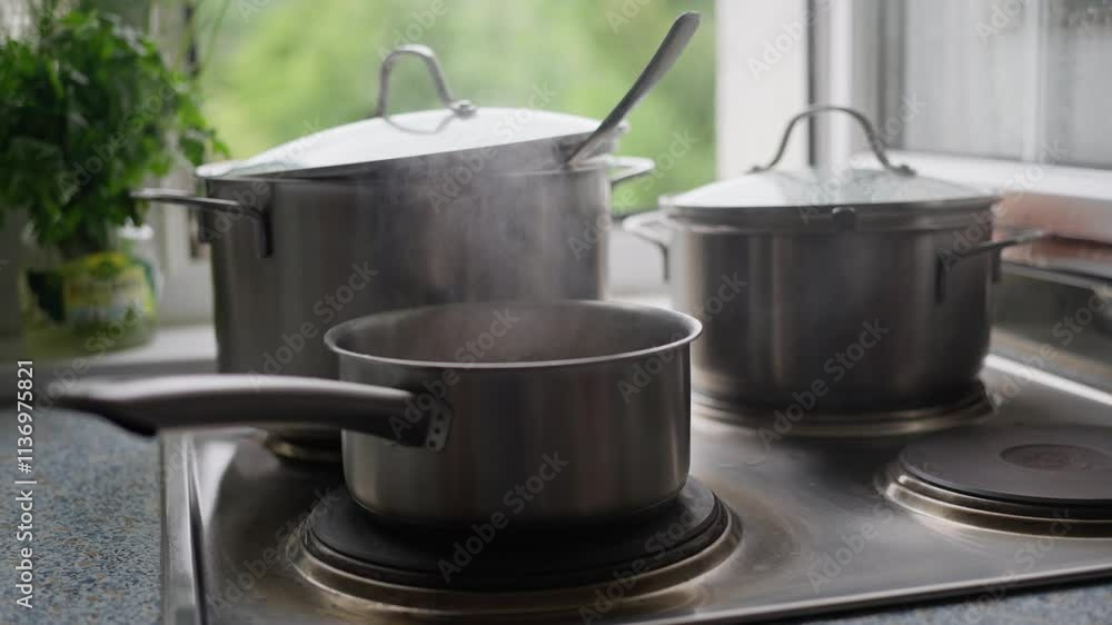 Steam gently rises from pots as they boil on the stove a fresh kitchen setting decorated with greenery outside. Slow motion Steam gently rises from pots as they boil on the stove a fresh kitchen setting decorated with greenery outside. Slow motion