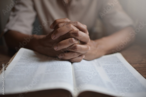 close up on the hands of an unrecognizable man reading the bible and praying. Concept of religiosity and mystery