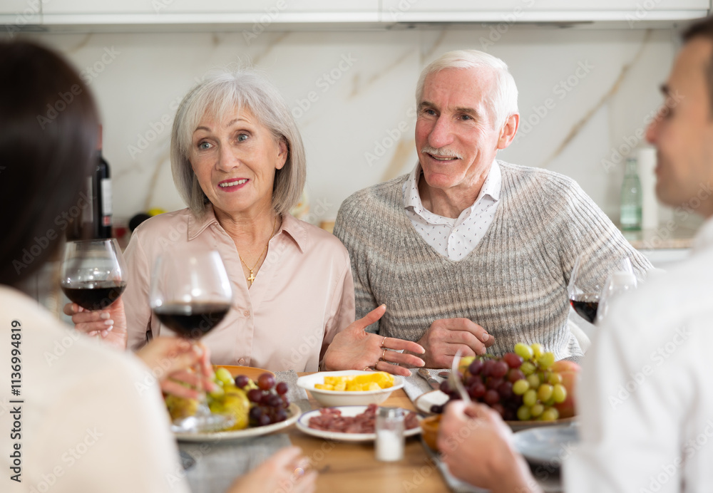 Mature spouses sitting at table, enjoying food and wine, chatting talking laughing with adult son and his girlfriend. In homely atmosphere male and female pensioner celebrate anniversary with guests Mature spouses sitting at table, enjoying food and wine, chatting talking laughing with adult son and his girlfriend. In homely atmosphere male and female pensioner celebrate anniversary with guests
