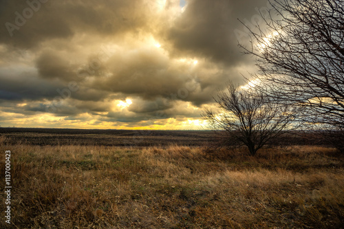 Big blue and orange clouds , over the field , sunlights through the clouds in the sky.Beautiful landscape on the field .Agriculture field and the sky.Sunset on the sky withot the sun.Orange sky nature photo